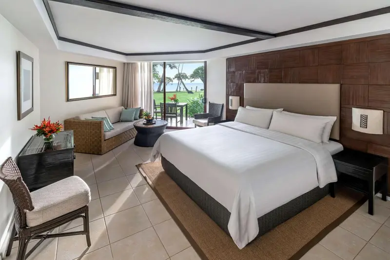Une chambre lumineuse avec un grand lit et un coin salon donnant sur une vue extérieure.