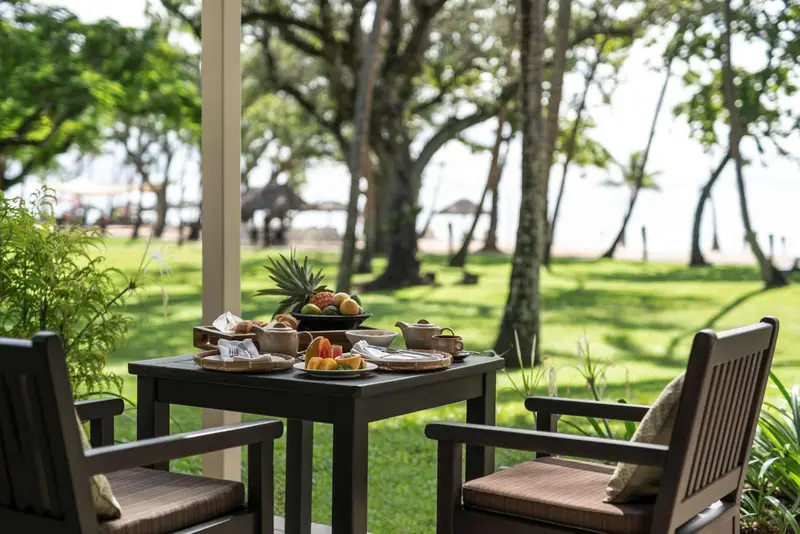 Une table est dressée pour le petit-déjeuner sur une terrasse ombragée.