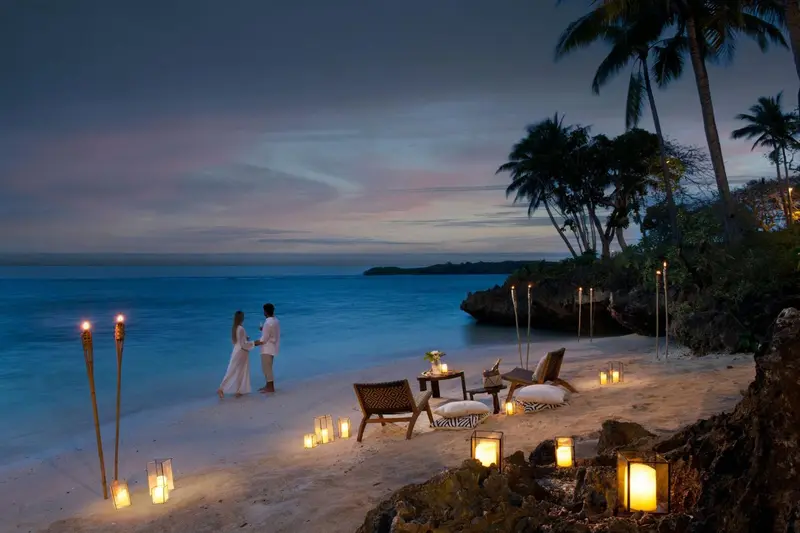 Un couple se tient sur une plage éclairée aux chandelles au coucher du soleil.