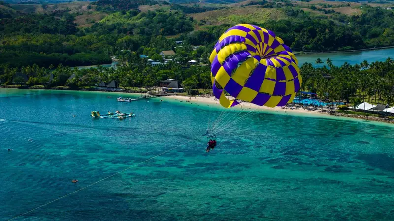 Une personne en parachute ascensionnel survole une plage tropicale.