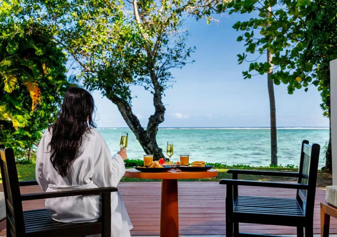 Une personne déguste une boisson et un petit-déjeuner sur une terrasse en bois face à la mer.