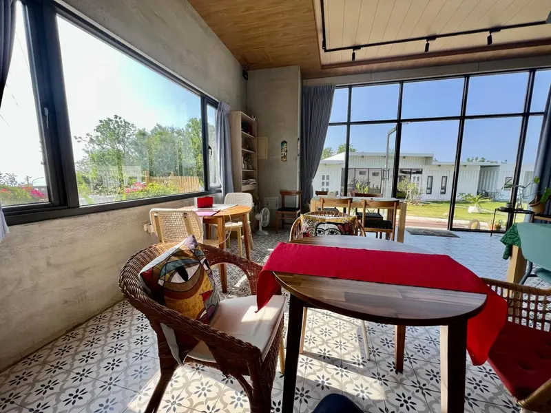 Une salle lumineuse s'ouvre sur une terrasse verdoyante avec des tables et des chaises.