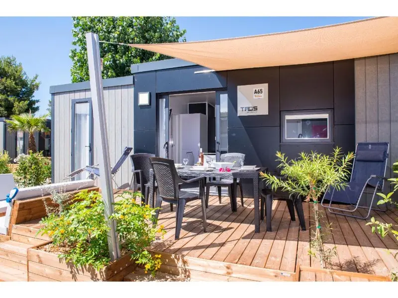 Terrasse aménagée avec table et chaises devant un bungalow sombre.