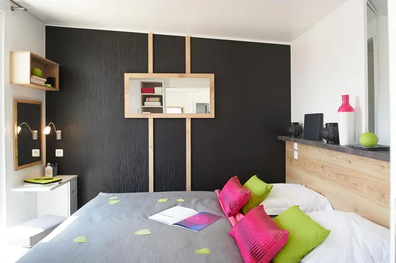 Une chambre à coucher avec un lit recouvert d'une couverture grise et de coussins colorés.