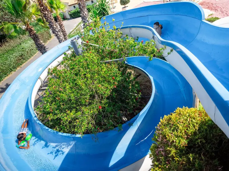 Toboggan aquatique bleu et blanc serpentant au milieu d'une végétation luxuriante.