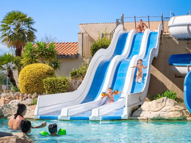 Des enfants glissent sur des toboggans aquatiques dans une piscine ensoleillée.