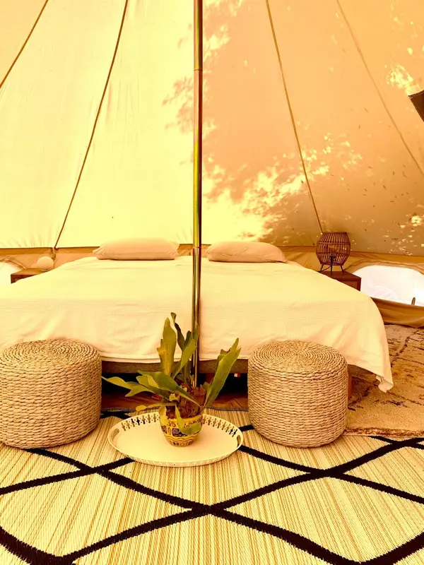 Lit recouvert de draps blancs dans une tente décorée de plantes.