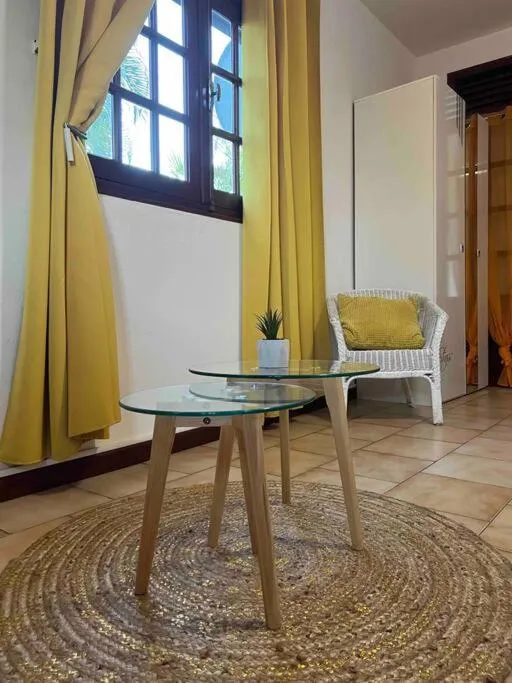 Une table basse en verre et bois est entourée d'un fauteuil en osier et d'un tapis rond.