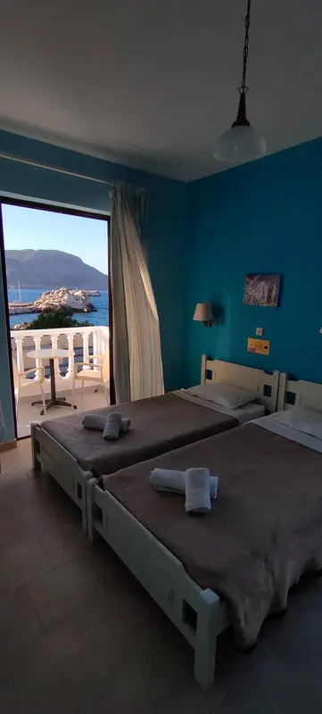Chambre lumineuse avec vue sur la mer depuis une porte-fenêtre ouverte.