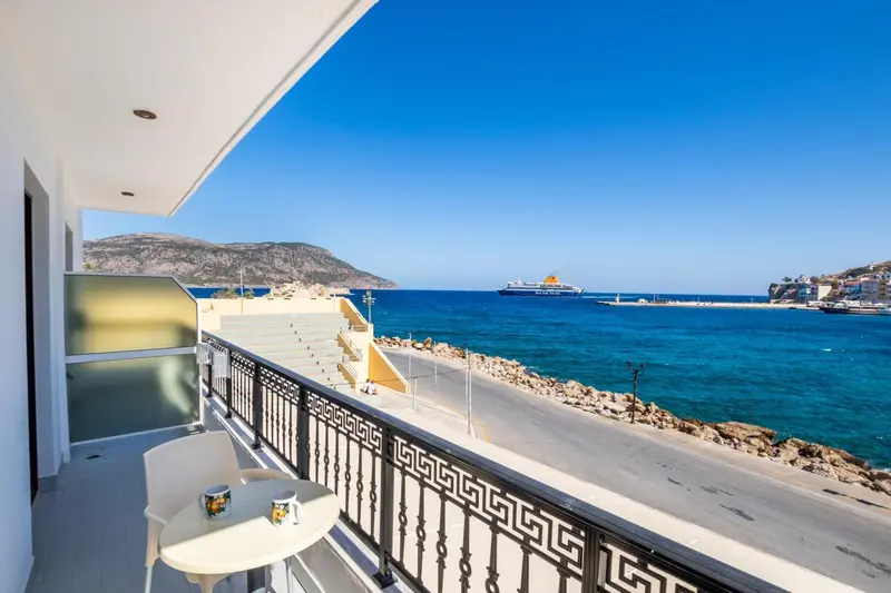 Vue d'un balcon avec une table et des chaises donnant sur la mer et un paysage montagneux.