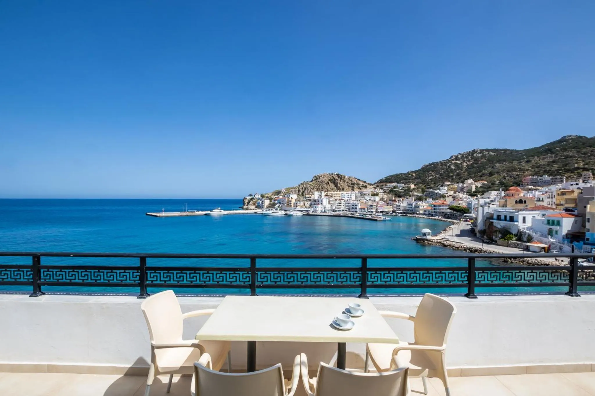 Vue sur la mer et la côte depuis une terrasse avec table et chaises.
