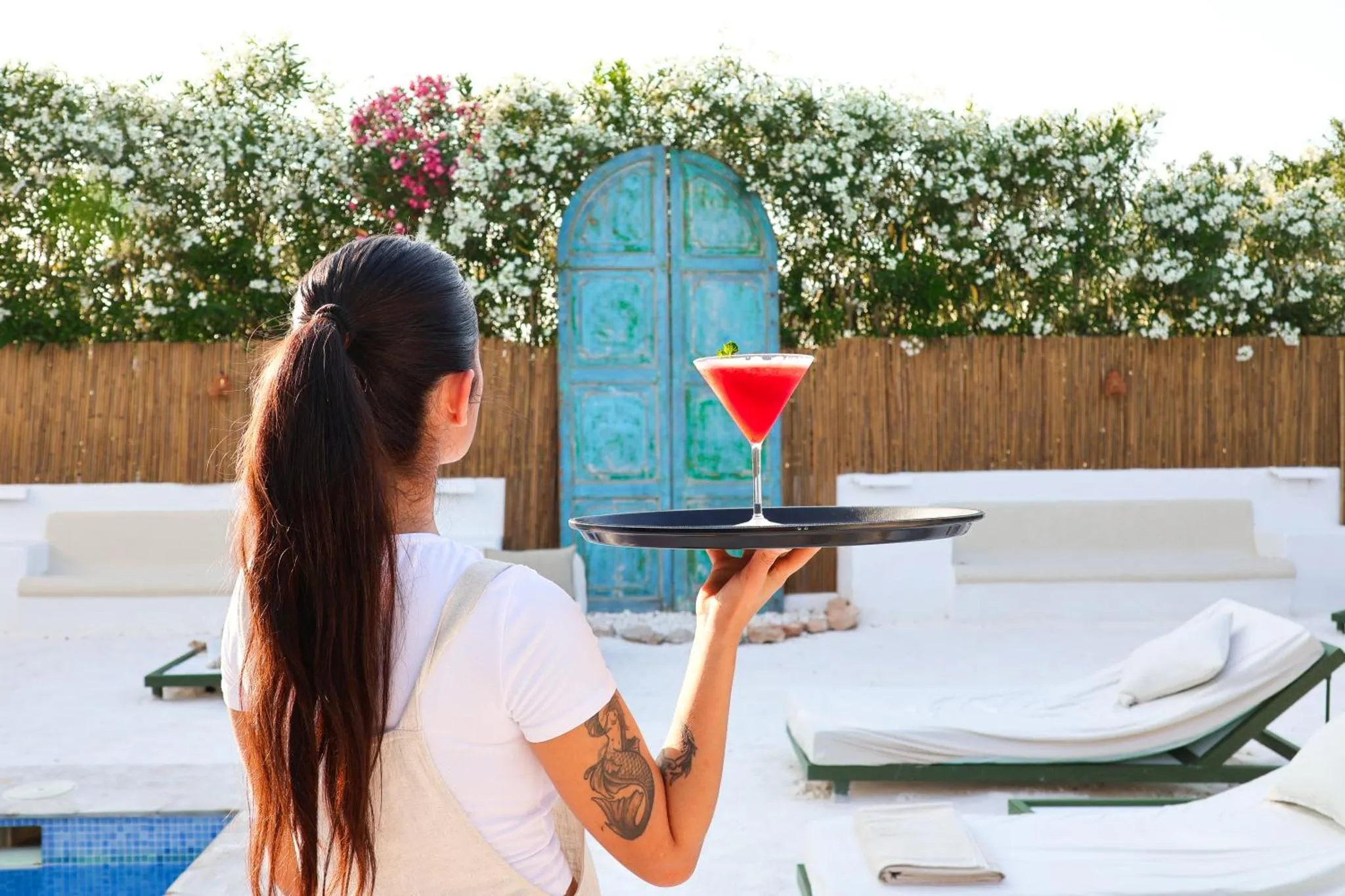 Une personne porte un cocktail devant une porte bleue et une piscine.