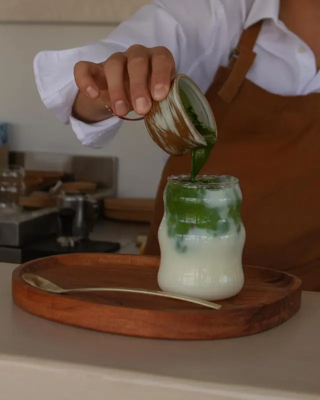 Une personne verse une boisson verte dans un verre rempli de liquide clair.