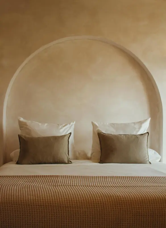 Un lit double avec des oreillers et une couverture est placé contre un mur beige avec une alcôve.