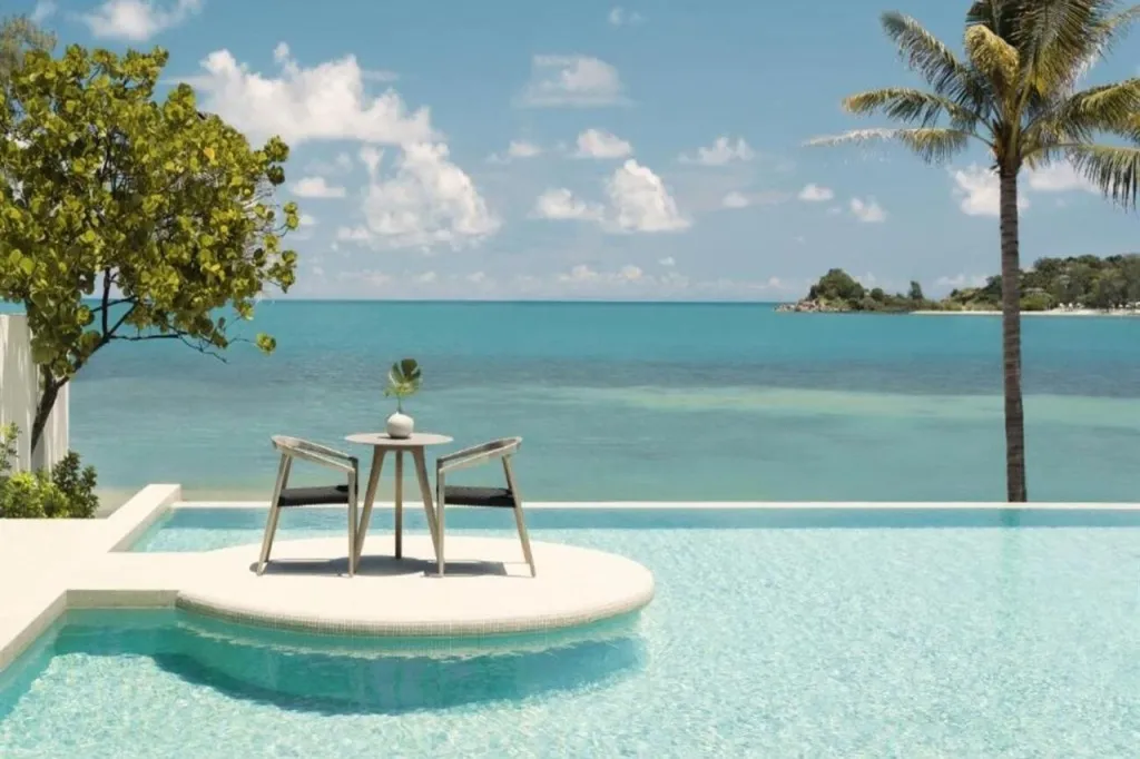 Deux fauteuils et une petite table se trouvent au bord d'une piscine à débordement avec vue sur la mer.