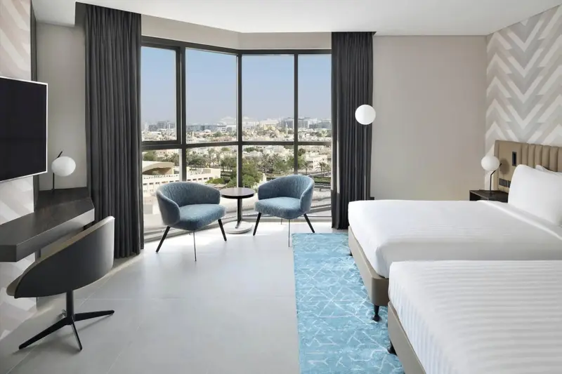 Une chambre lumineuse avec un bureau, deux fauteuils et une vue sur la ville.