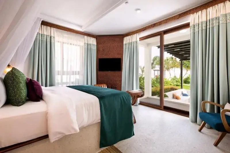 Une chambre lumineuse avec un lit recouvert d'un plaid vert et un accès à une terrasse.