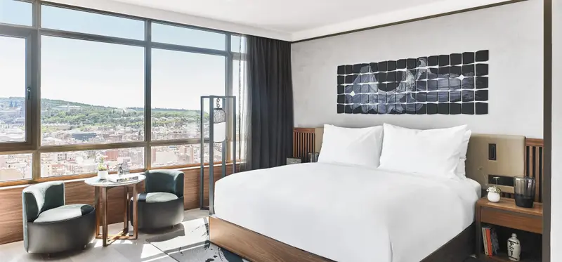 Une chambre lumineuse avec un grand lit et un coin salon près d'une fenêtre panoramique.