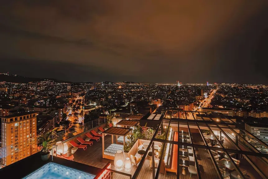 Vue nocturne sur une ville illuminée depuis un espace aménagé avec piscine et mobilier de détente.