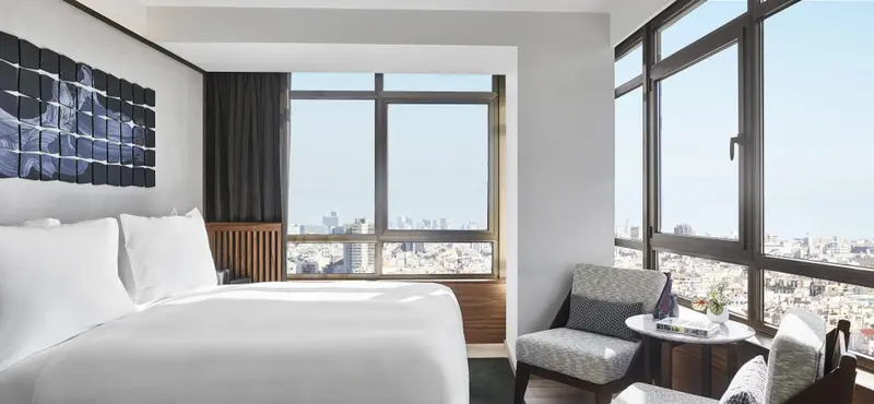 Une chambre lumineuse avec un lit blanc et deux fauteuils près d'une grande fenêtre.