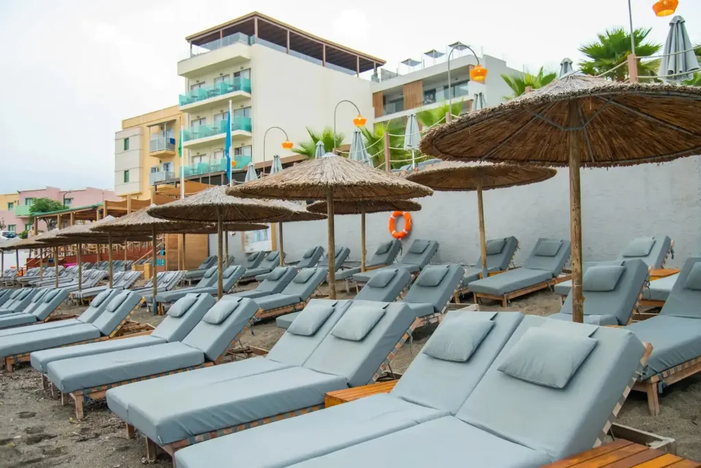 Transats et parasols sur une plage de sable sombre devant un bâtiment.