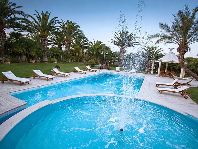 Une piscine rectangulaire avec une fontaine centrale et des transats blancs.
