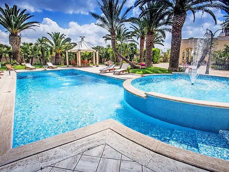 Une piscine bleue avec des transats et un gazebo dans un jardin luxuriant.
