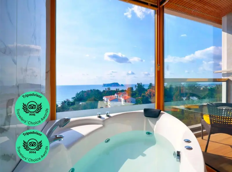 Un jacuzzi est installé devant une grande baie vitrée offrant une vue sur la mer et le paysage.