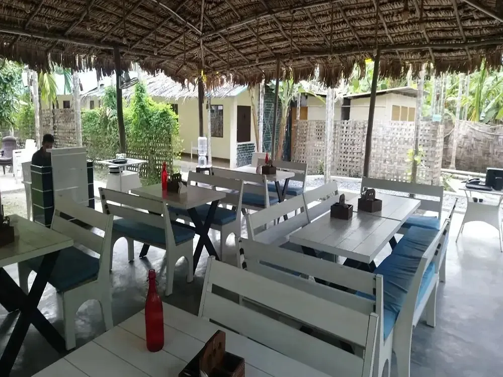 Une salle à manger extérieure abritée sous une toiture de chaume avec des tables et des bancs en bois.