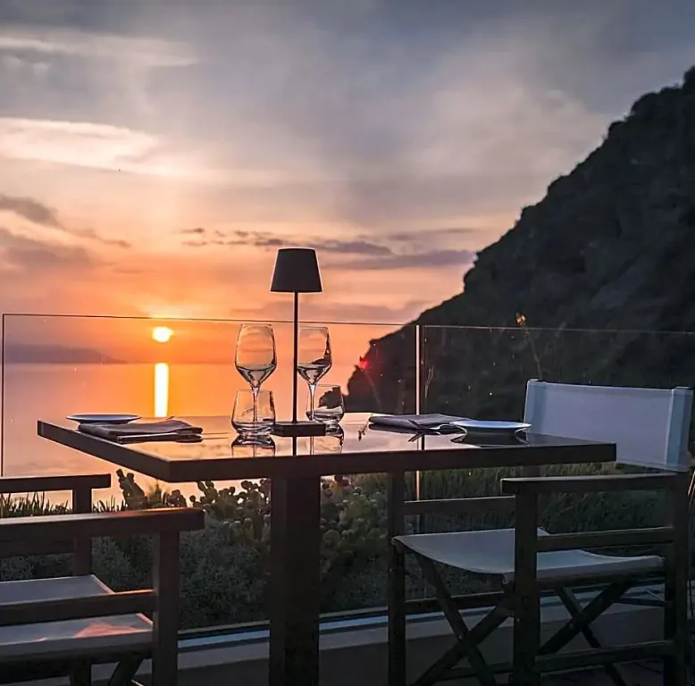 Une table est dressée en terrasse avec vue sur la mer au coucher du soleil.