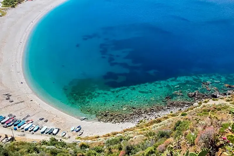 Une plage de galets bordée d'une eau turquoise et d'une végétation luxuriante.