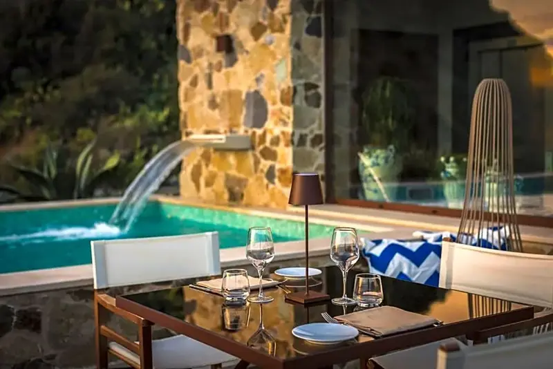 Une table est dressée devant une piscine avec une cascade artificielle.