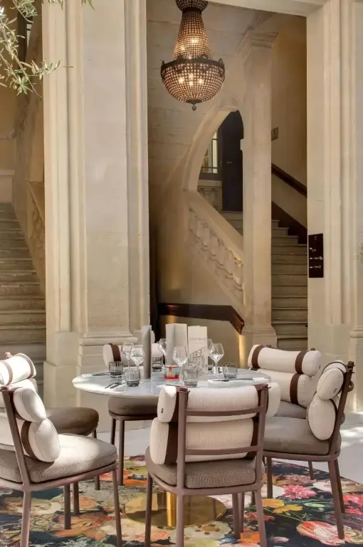 Une table ronde est dressée dans un espace lumineux avec un escalier en pierre en arrière-plan.