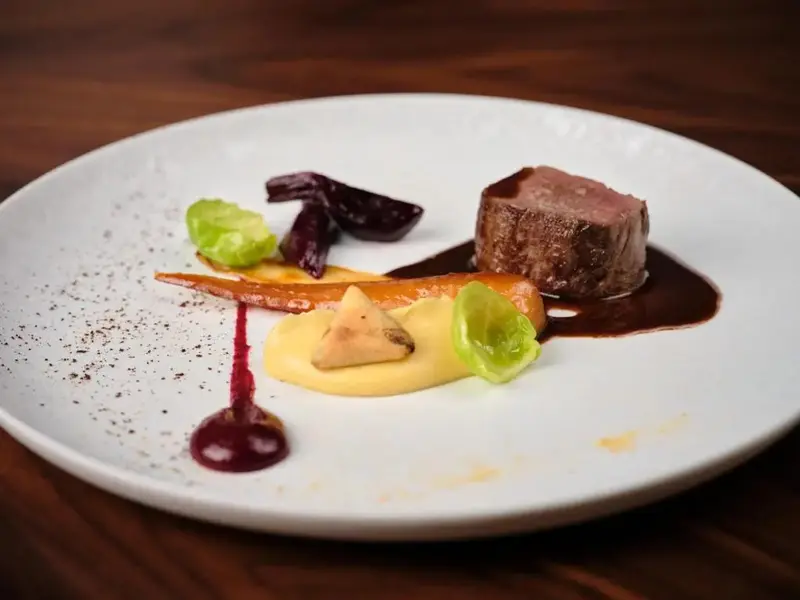 Assiette raffinée avec une portion de viande, des légumes et une sauce.