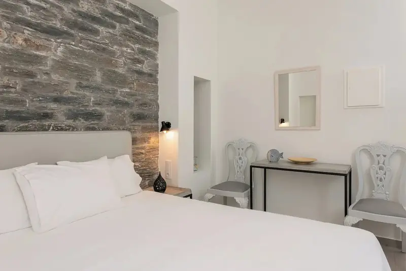 Une chambre lumineuse avec un grand lit et un mur en pierre.