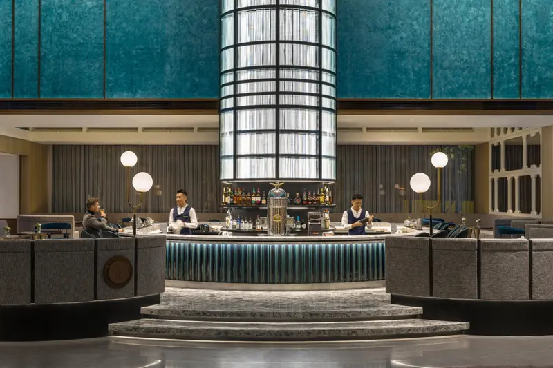 Un bar élégant avec un comptoir central et des clients assis sur des banquettes.