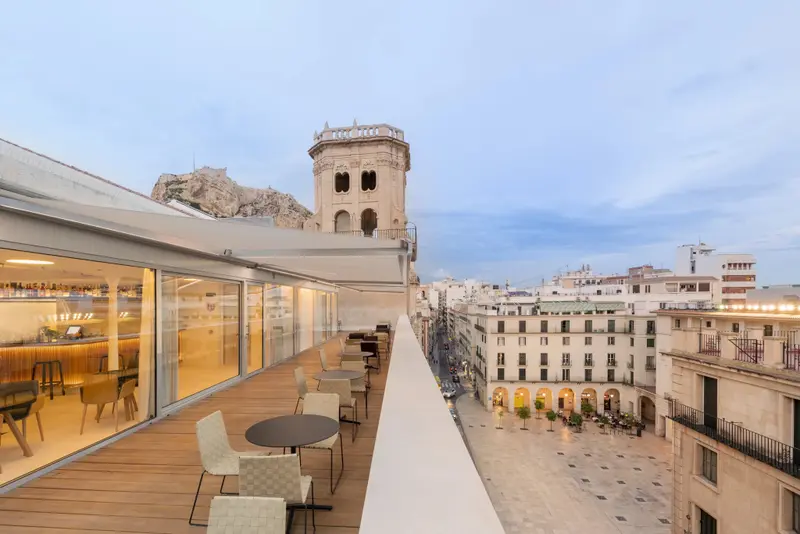 Terrasse aménagée avec tables et chaises offrant une vue sur la ville et un monument historique.