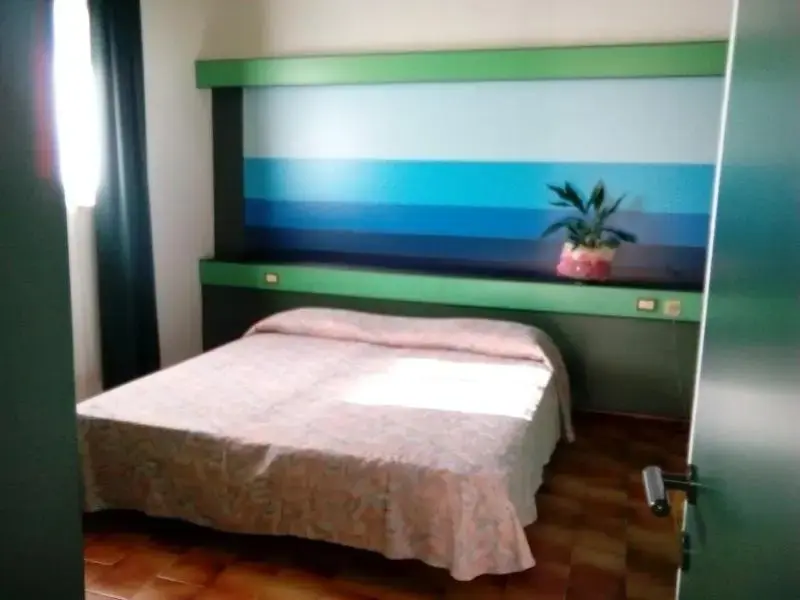 Une chambre lumineuse avec un lit recouvert d'une couverture claire et une décoration murale abstraite.