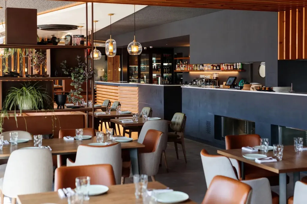 Une salle de restaurant lumineuse avec des tables dressées et un comptoir de bar.