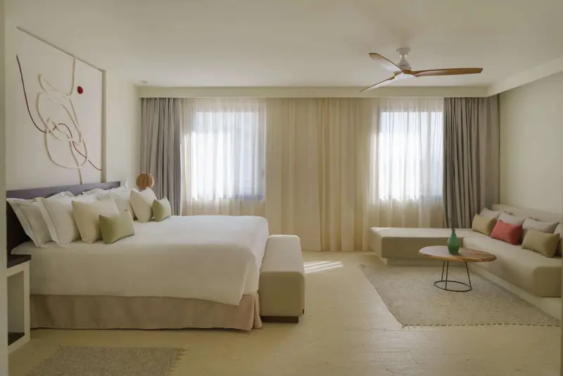 Une chambre lumineuse avec un grand lit et un espace salon.