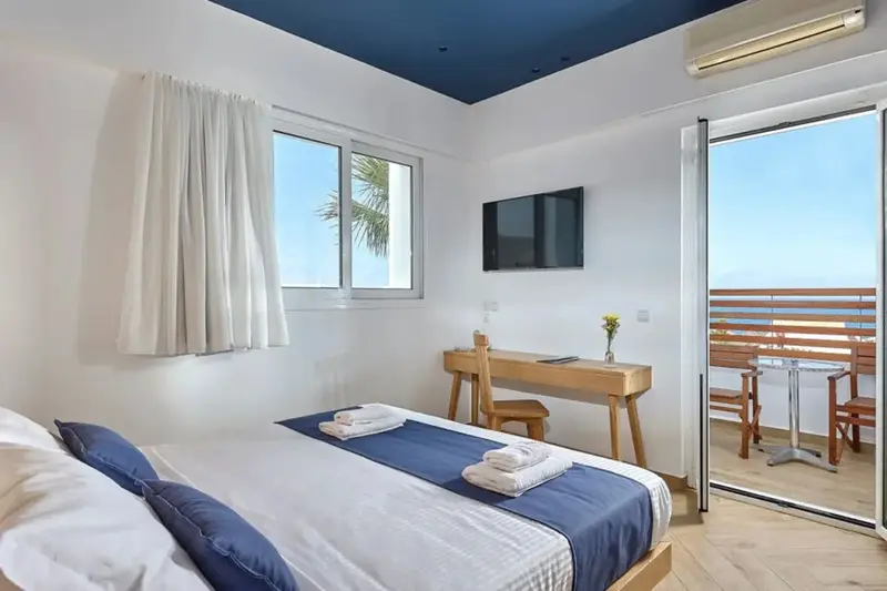 Une chambre lumineuse avec un lit fait et un bureau donnant sur une terrasse.