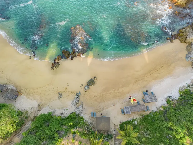 Vue aérienne d'une plage de sable fin bordée d'une eau turquoise et d'une végétation luxuriante.