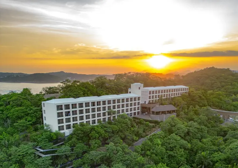 Bâtiment blanc moderne entouré d'une végétation luxuriante au coucher du soleil.