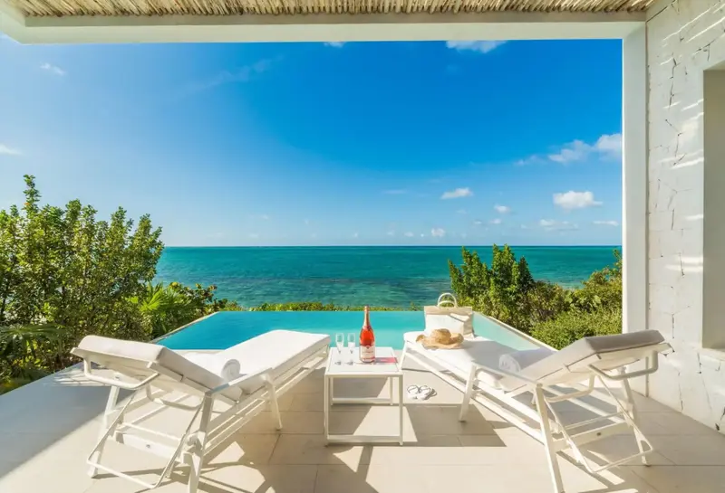 Deux chaises longues blanches bordent une piscine à débordement avec vue sur la mer turquoise.
