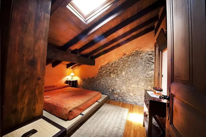 Une chambre aux murs en pierre et au plafond en bois présente un lit recouvert d'une courtepointe.