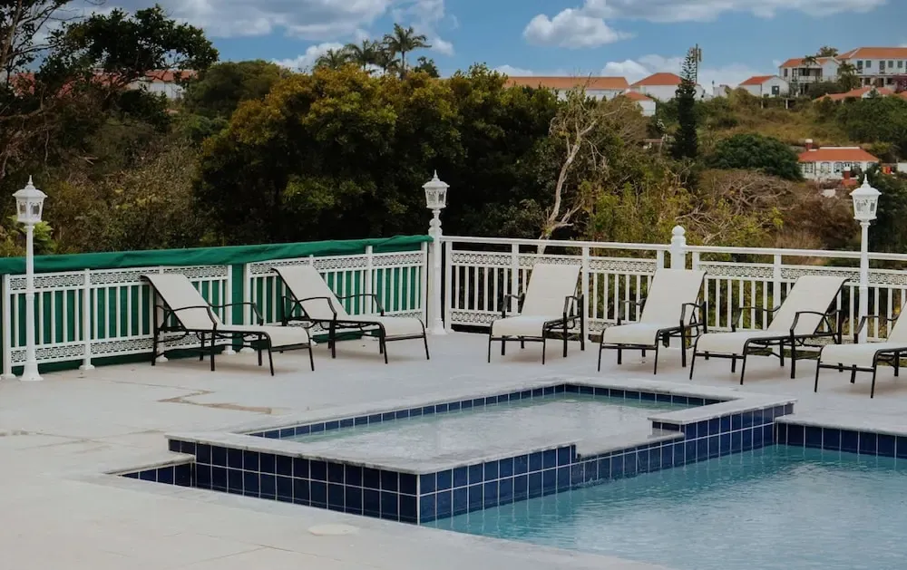 Transats blancs disposés autour d'une piscine ensoleillée avec une végétation luxuriante en arrière-plan.