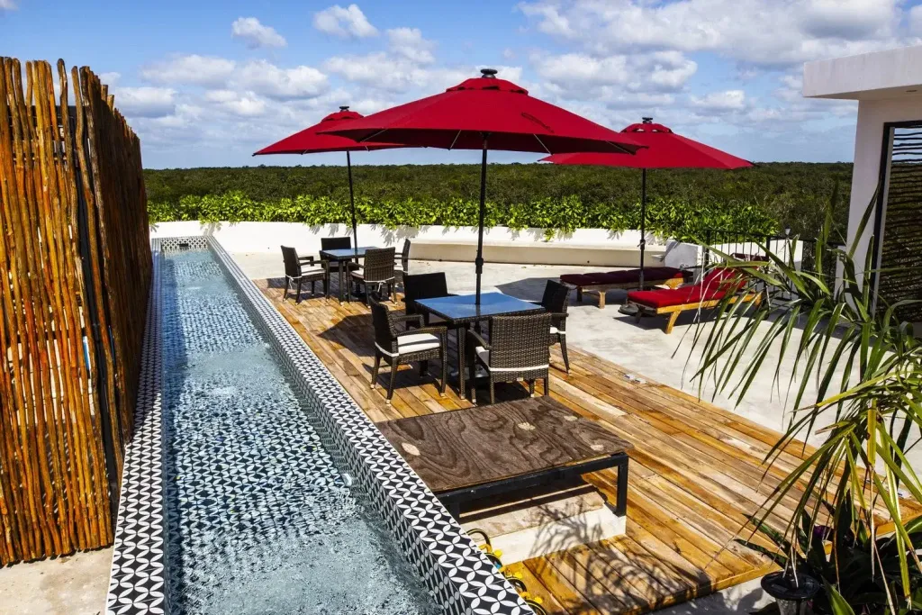 Terrasse aménagée avec tables, chaises et parasols rouges près d'une piscine étroite.