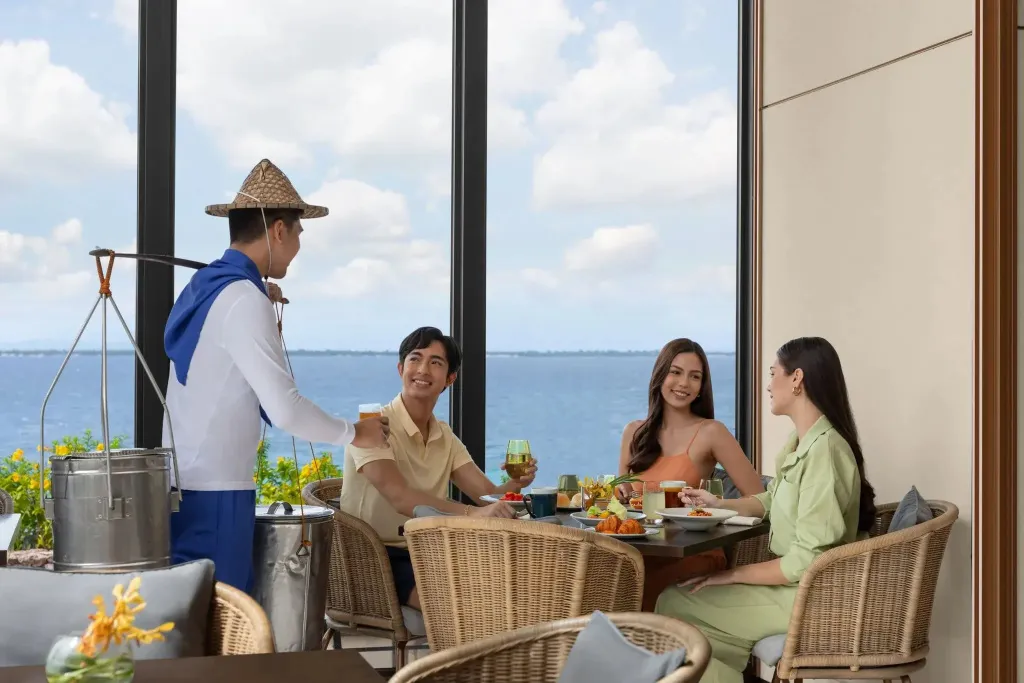 Des convives sont servis à table dans une salle lumineuse avec vue sur la mer.