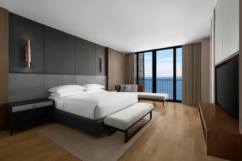 Une chambre lumineuse avec un grand lit et un accès à un balcon avec vue sur la mer.