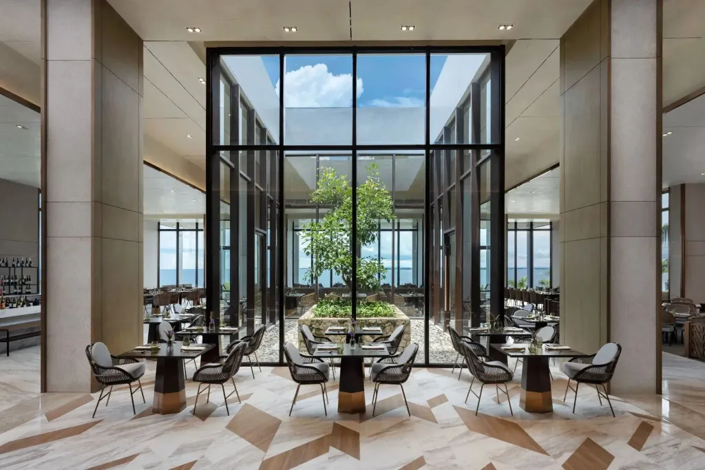 Une salle à manger lumineuse avec de grandes baies vitrées donnant sur une cour intérieure verdoyante.